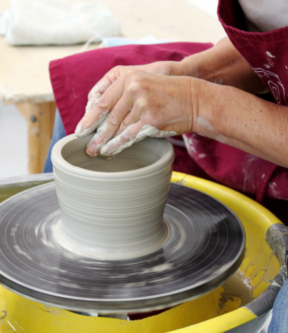 Auf dem Bild sind Hände einer Frau zu sehen, die ein Gefäß aus Ton auf einer Scheibe dreht. Auf dem Bild sind Hände einer Frau zu sehen, die ein Gefäß aus Ton auf einer Scheibe dreht.