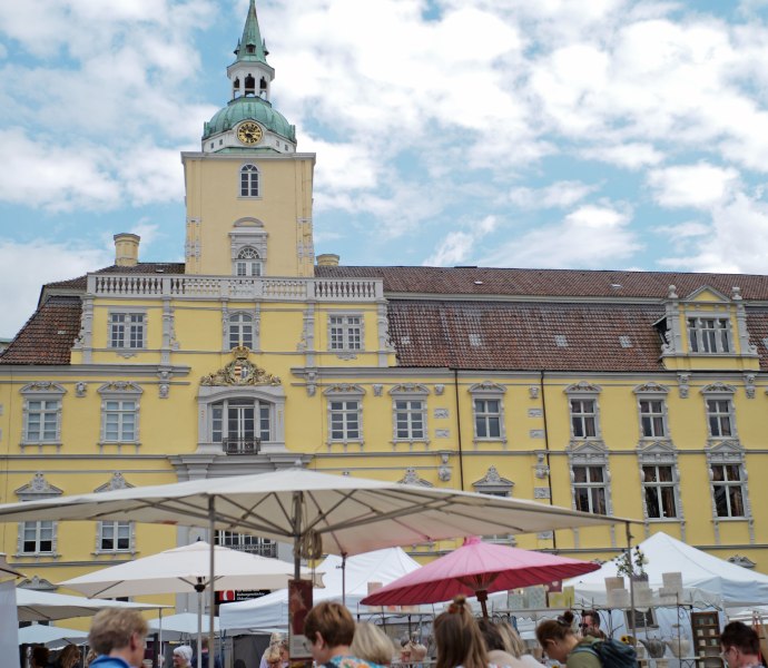 Das Bild zeigt einen Keramikmarkt, auf dem sich evrschieden Menschen Keramik ansehen, vor dem Oldenburger Schloss als Kulisse.
